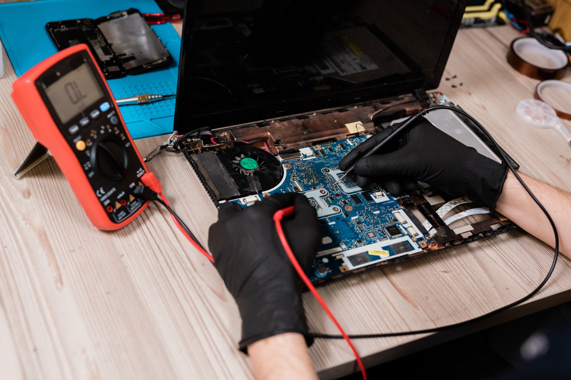 Master of repair service using soldering-irons while working over broken laptop